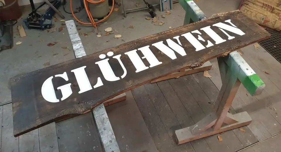 A long rustic oak sign painted with the word Glühwein