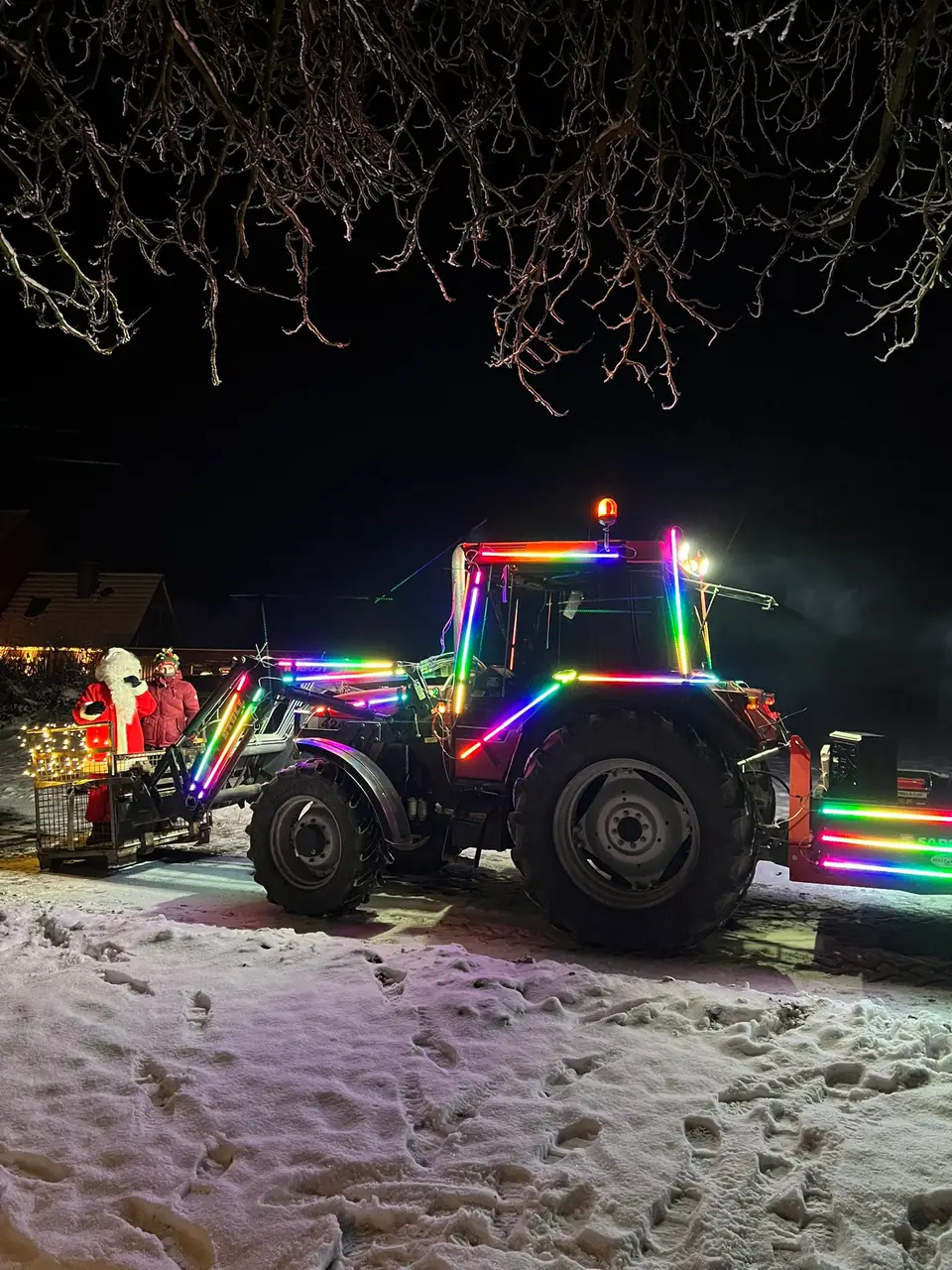 A tractor covered in colorful lights at a snowy nighttime event
